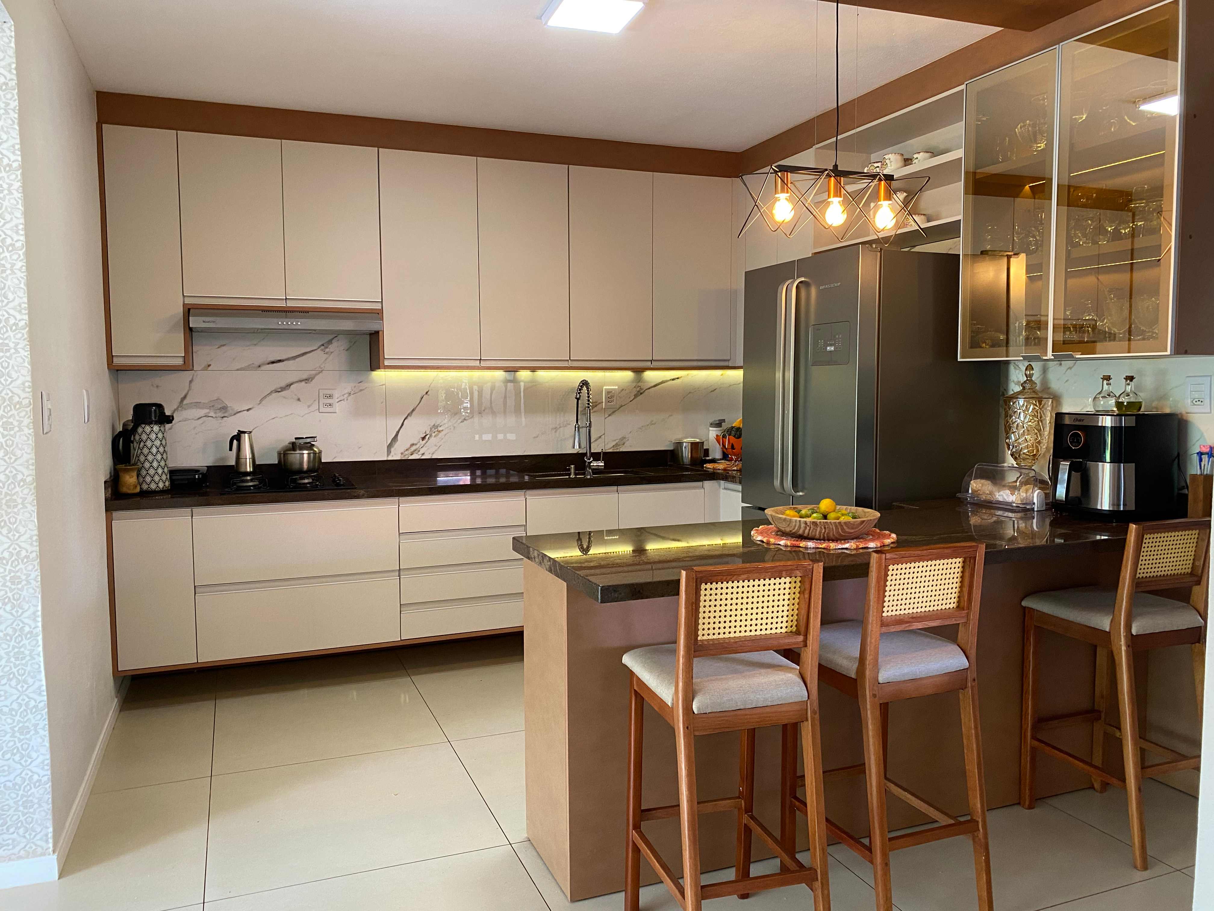 Cozinha planejada completa Karol Móveis Santa Rosa RS - armários em tons bege com detalhes em madeira, bancada em granito, ilha com banquetas e cristaleira com iluminação LED